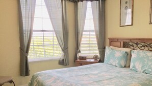 Un dormitorio con cama, cortinas, una mesita de noche y una ventana con persianas.