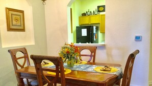 Una mesa de comedor con cuatro sillas, un florero con flores y una cocina visible a través de un arco.