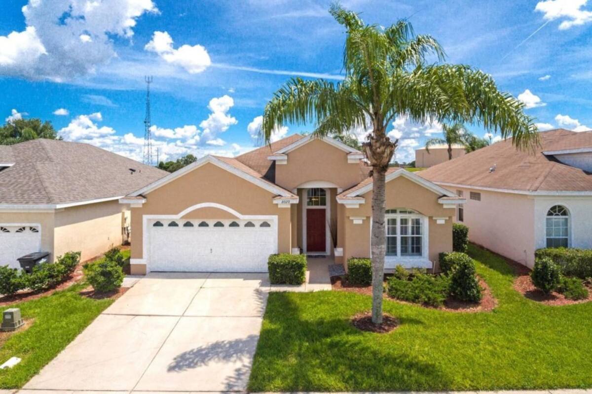 A single-story house with a garage, a front yard with a palm tree, and a clear blue sky.