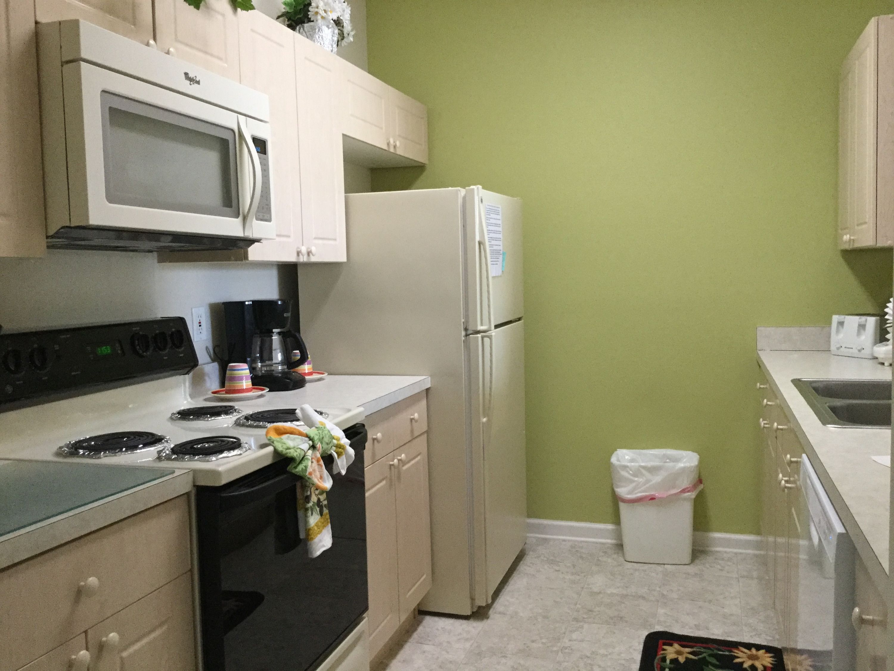 A compact kitchen with a microwave, stove, refrigerator, and a trash bin.