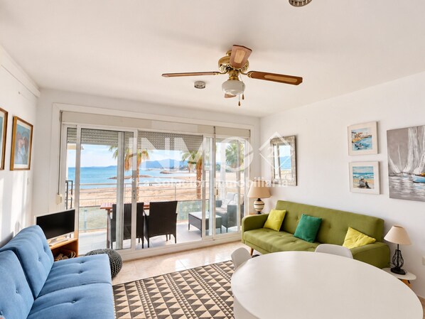 A modern living room with a view of the beach, a ceiling fan, and a green sofa.