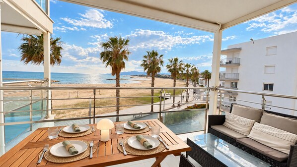 Un balcón con una mesa de comedor lista para dos personas, con vista a una playa y al océano.