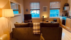 Una sala de estar con sofá, televisor, lámpara y una cocina con microondas y estufa.