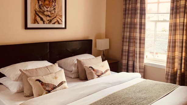 Una cama bien hecha con cabecera, un cuadro enmarcado de un tigre y una ventana con cortinas.