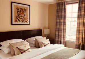 A neatly made bed with a headboard, a framed tiger painting, and a window with curtains.