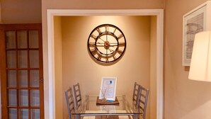 Un comedor con una mesa de vidrio, sillas de metal, un reloj de pared y un menú enmarcado sobre la mesa.