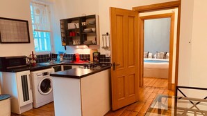 A compact kitchen with a washing machine, a stove, and a dining area with a glass table.