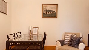 A dining area with a glass-top table, four chairs, a framed certificate, and a painting on the wall.