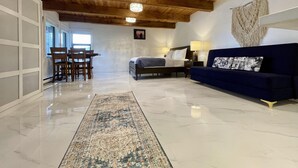 A spacious room with a wooden ceiling, a bed, a blue sofa, and a dining area with chairs and a table. - A Room With a View (Ucluelet)