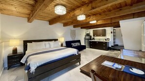A bedroom with a bed, bedside tables, a desk, and a kitchenette in the background. - A Room With a View (Ucluelet)