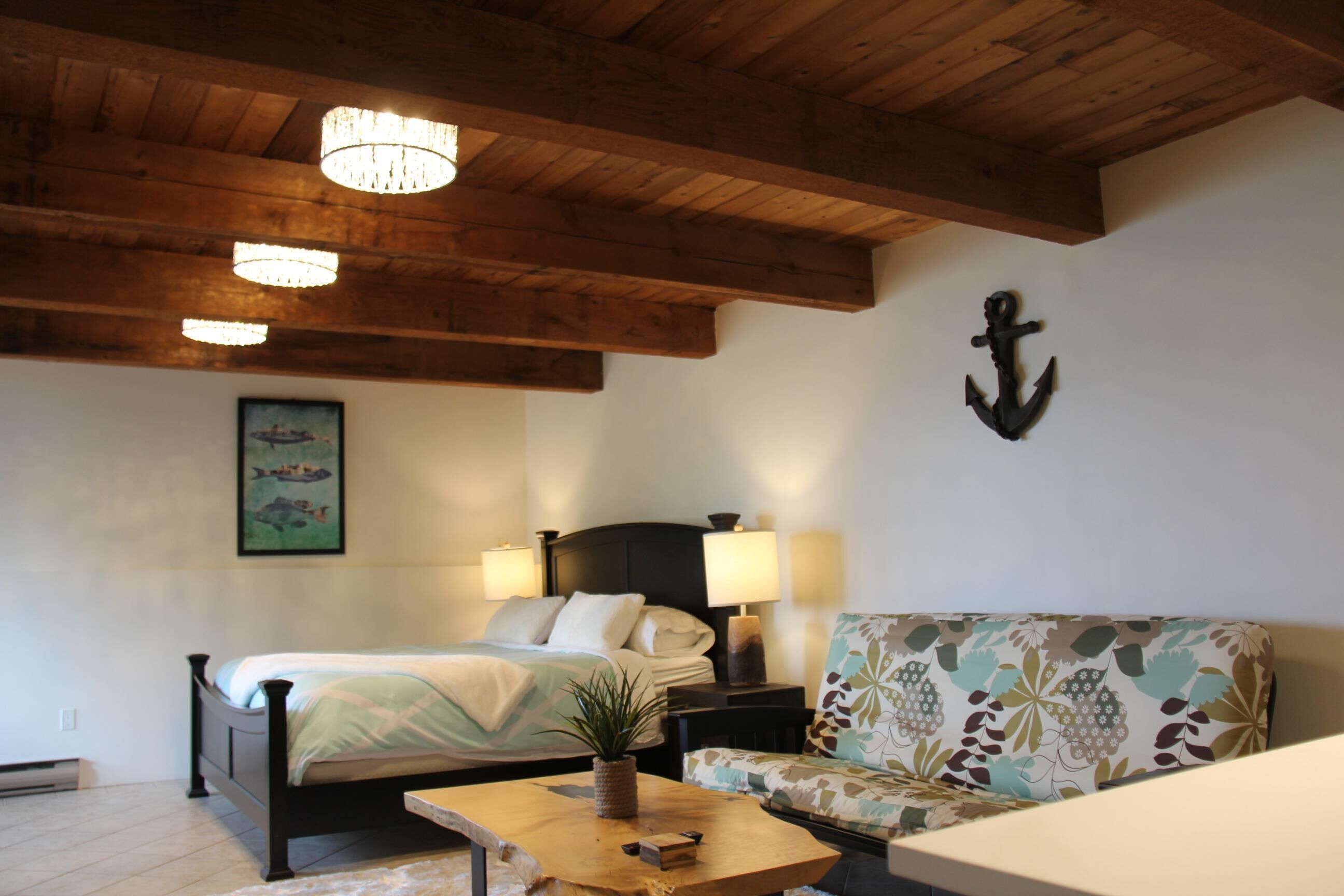 A bedroom with a bed, bedside lamps, a wooden ceiling, a wall-mounted anchor decoration, and a framed picture.