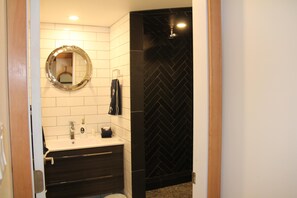 A bathroom with a white tiled wall, a black herringbone-patterned shower wall, a round mirror, a sink with a faucet, and a towel hanging on the wall. - A Room With a View (Ucluelet)