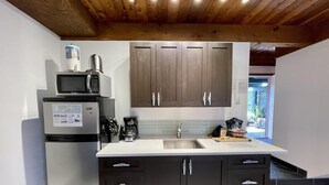 A modern kitchen with dark cabinets, a stainless steel refrigerator, a microwave, and a coffee maker. - A Room With a View (Ucluelet)