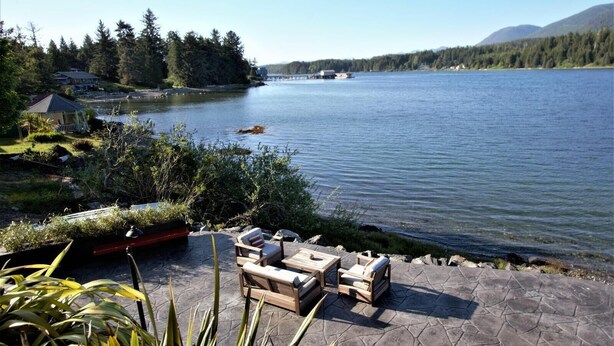 A waterfront patio with outdoor furniture and a view of a lake and forested hills. - A Room With a View (Ucluelet)