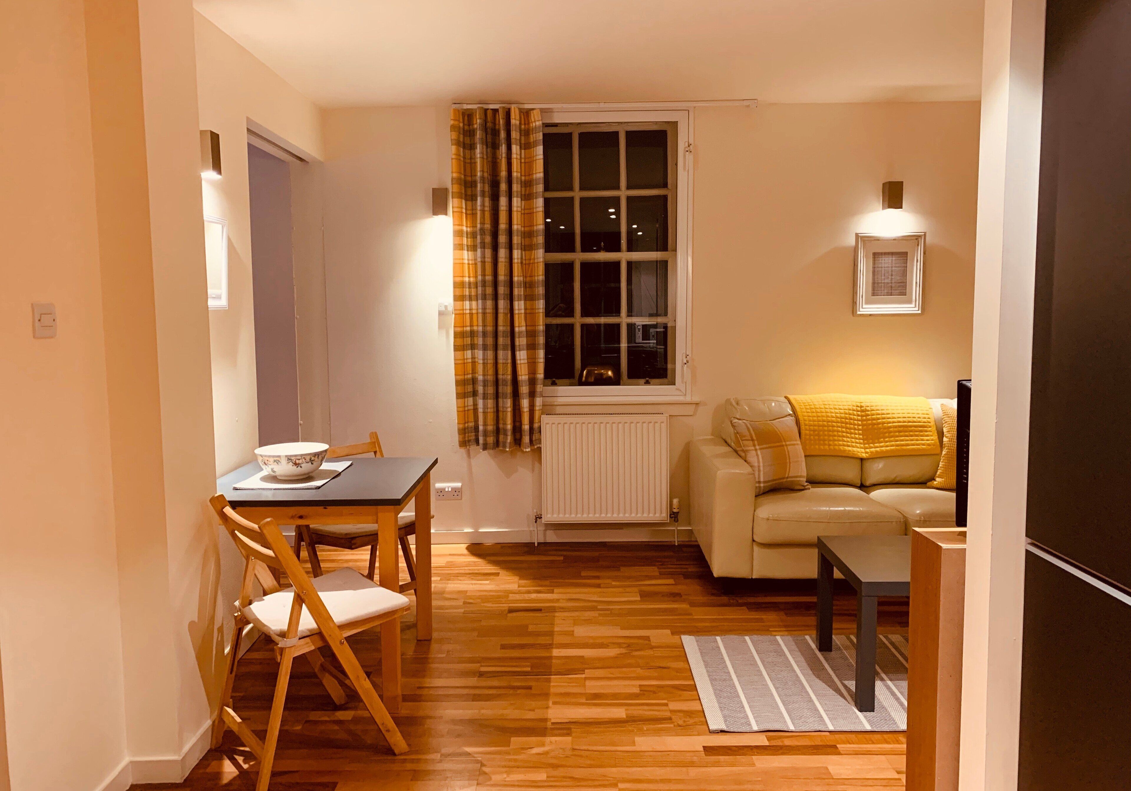Un espacio habitable compacto con zona de comedor, sofá, radiador y ventana con cortinas.