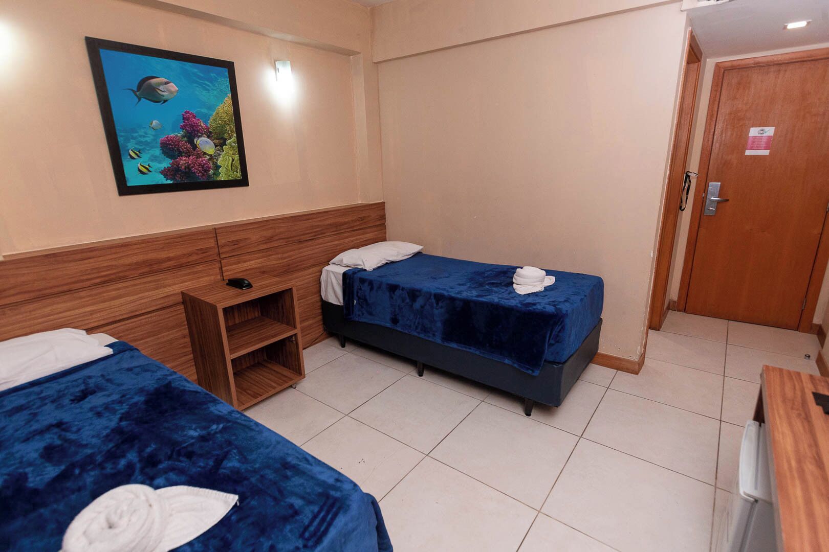 A hotel room with two beds, a wooden headboard, a small desk, and a painting of an underwater scene.