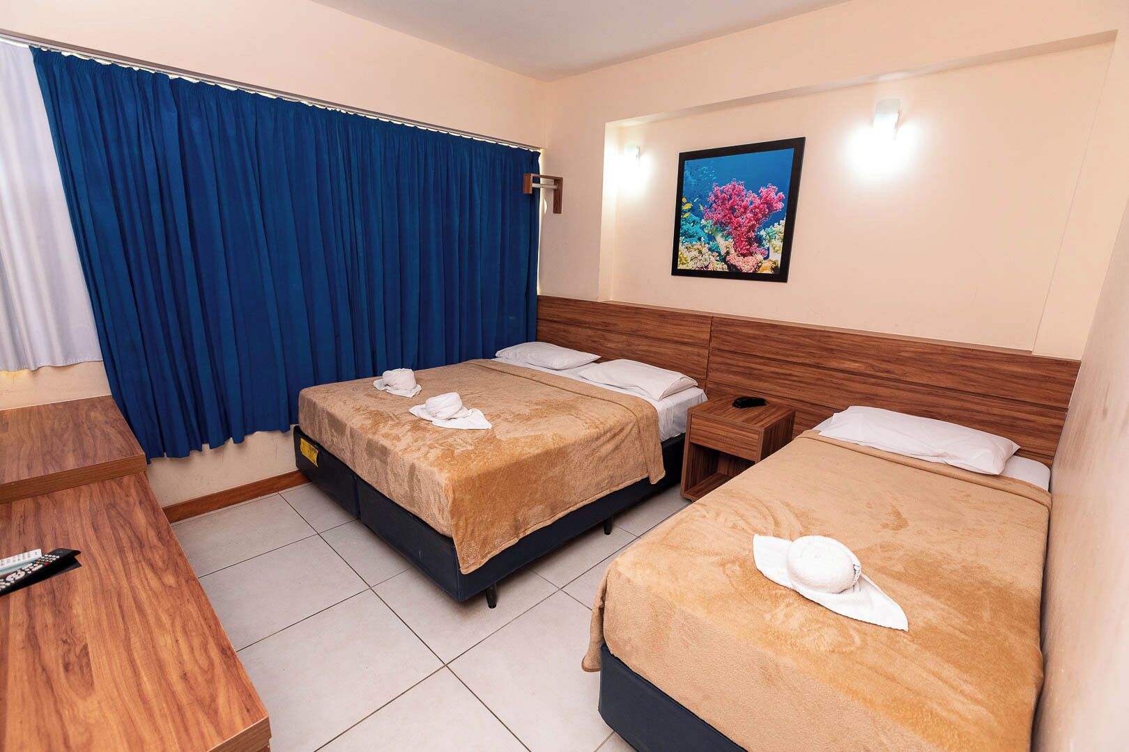 Una habitación de hotel con dos camas, un escritorio de madera, una mesita de noche y un cuadro de un arrecife de coral en la pared.