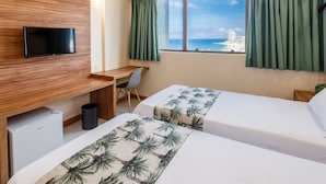 Ett hotellrum med två sängar, ett skrivbord, en tv och utsikt över havet.