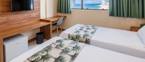 Habitación de hotel con dos camas, un escritorio, televisión y vista al océano.