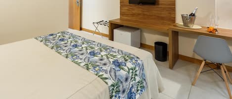 Habitación de hotel con cama, escritorio, televisor, minibar y una silla.