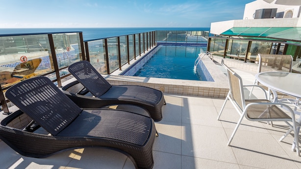 En pool på taket med två solstolar och ett bord, med utsikt över havet.