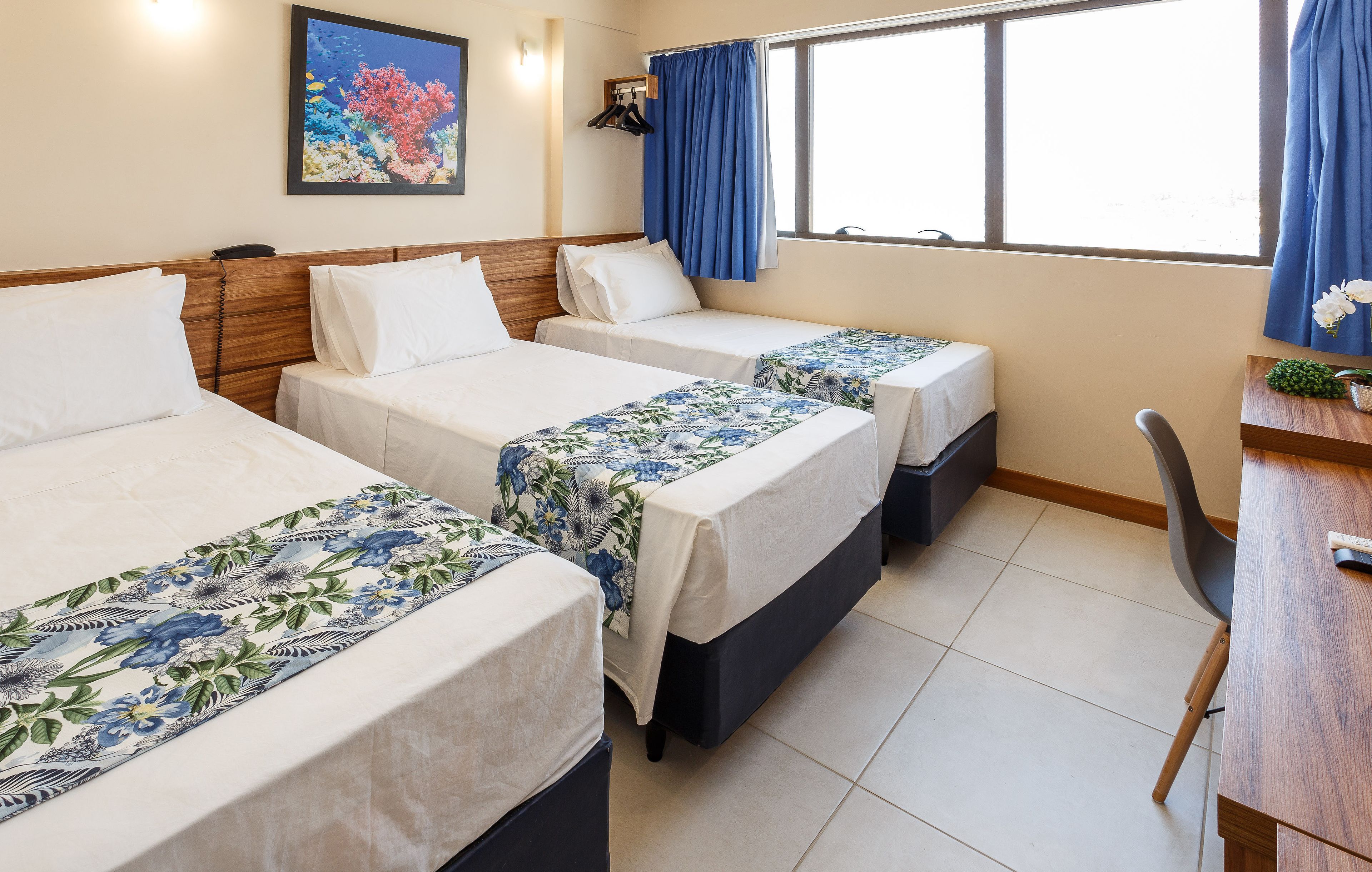 A hotel room with three beds, a desk, and a chair.