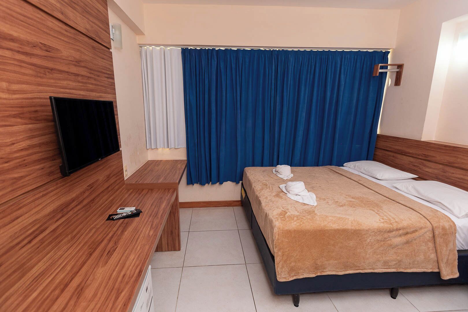 Une chambre d’hôtel avec un lit, une télévision, un banc en bois et un rideau.