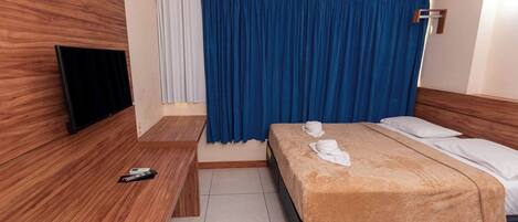 Une chambre d’hôtel avec un lit, une télévision, un banc en bois et un rideau.