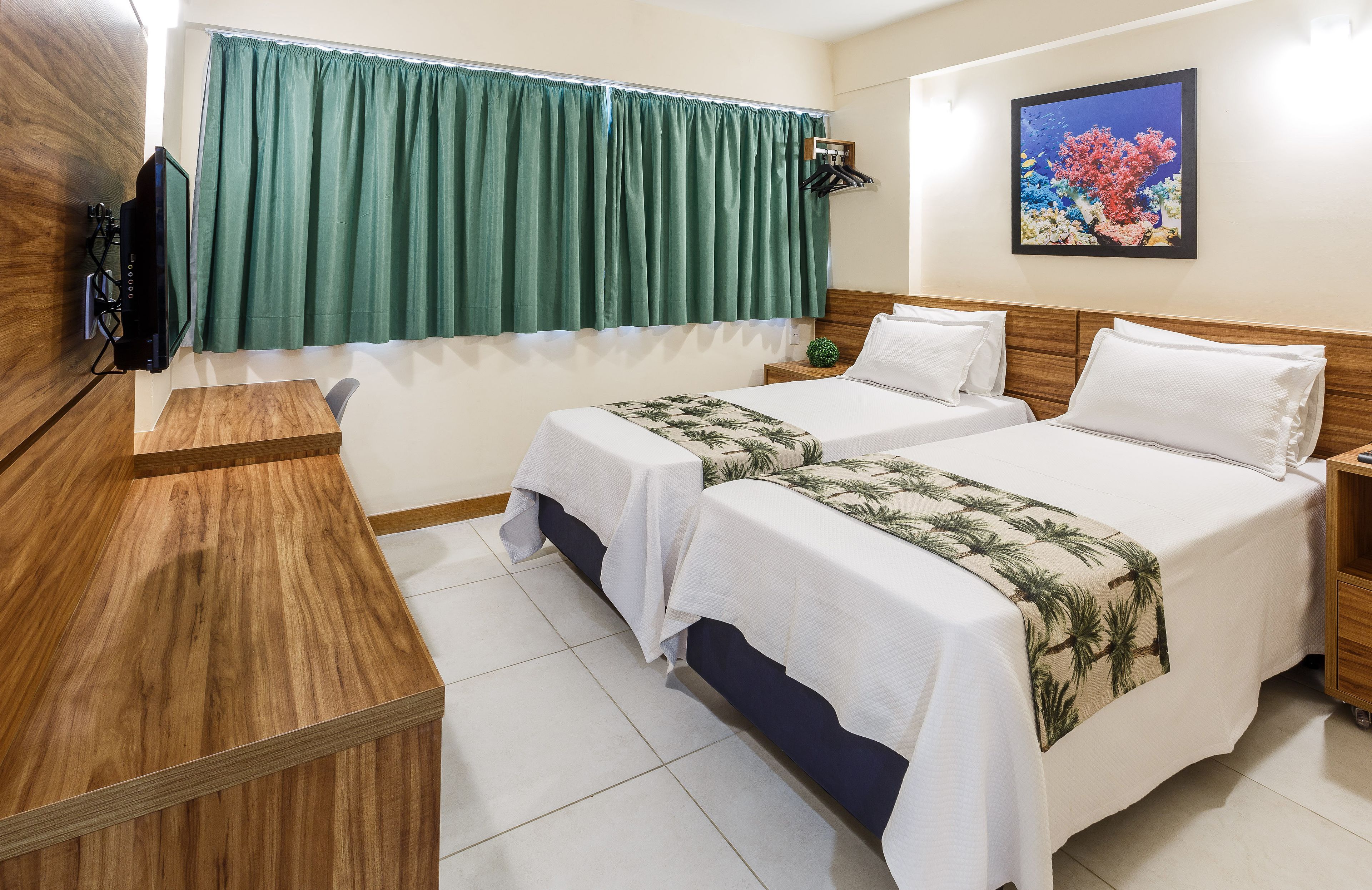 Een hotelkamer met twee bedden, een houten bureau, een televisie en een groen gordijn.