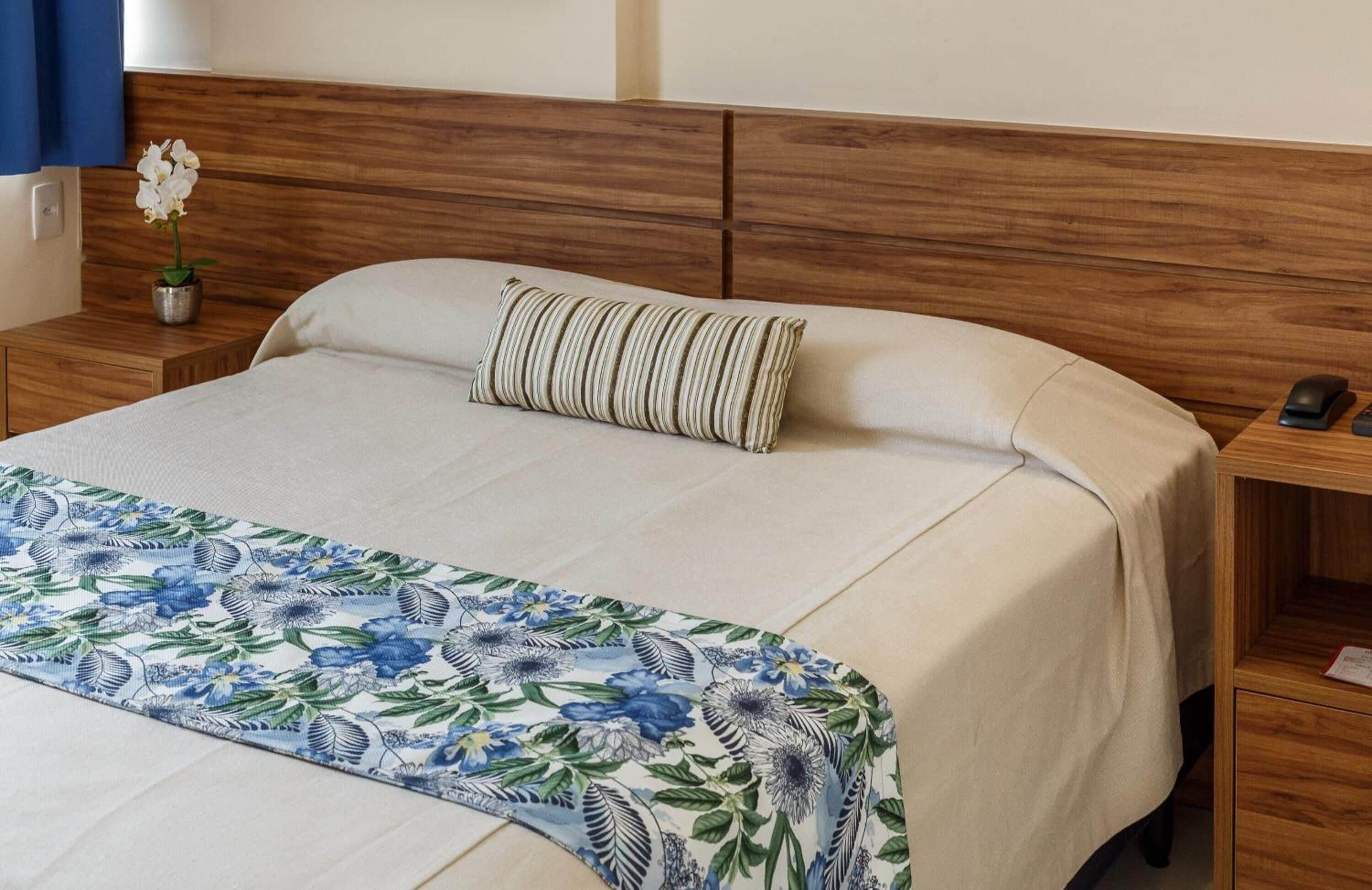A neatly made bed with a floral bedspread, a striped pillow, and a small potted orchid on a wooden nightstand.