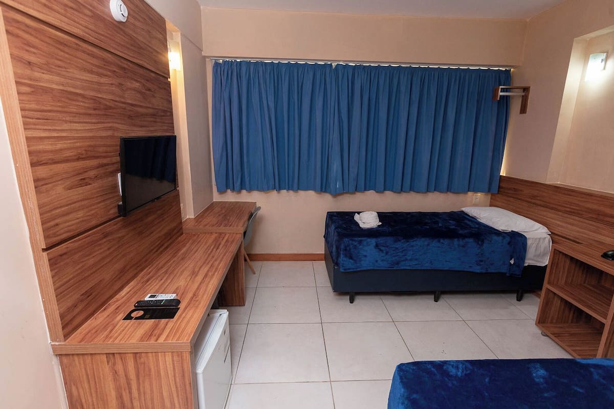 A compact room with a bed, a desk, a chair, a TV, and a window with curtains.
