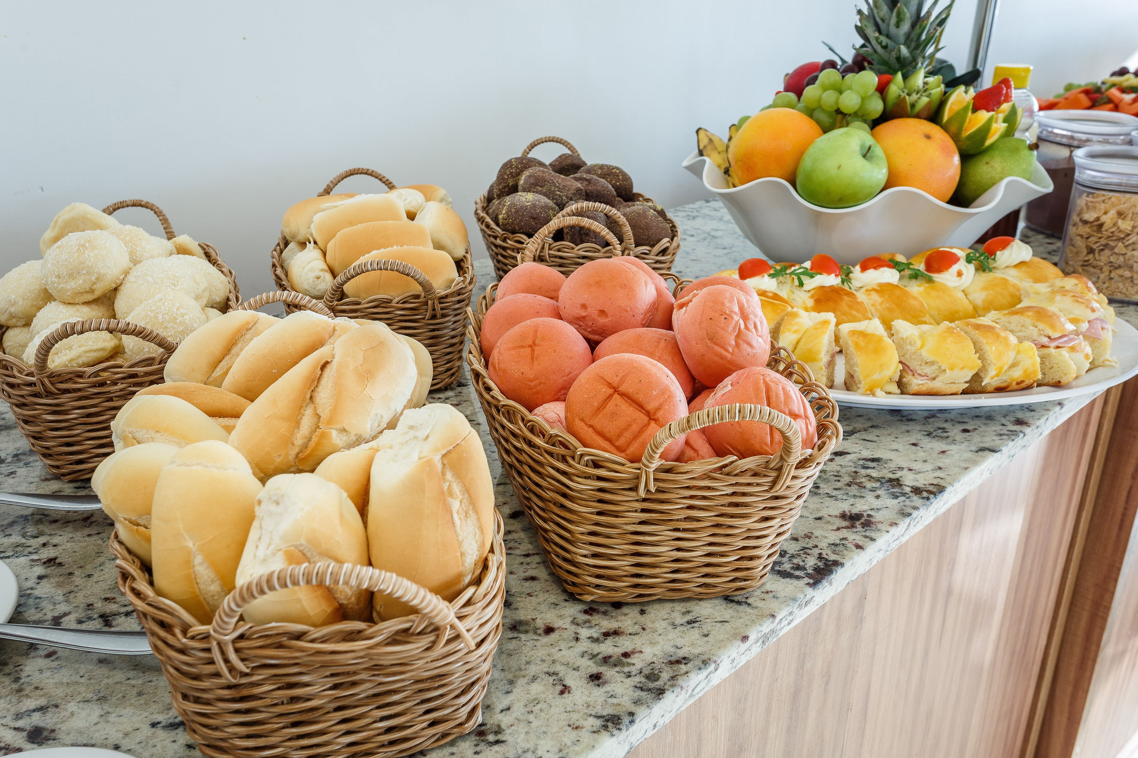 Una mesa de buffet con diversos alimentos, incluyendo panes, pasteles y un bol de fruta.