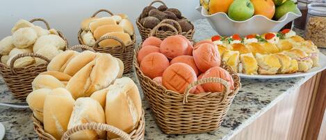 Una mesa de buffet con diversos alimentos, incluyendo panes, pasteles y un bol de fruta.