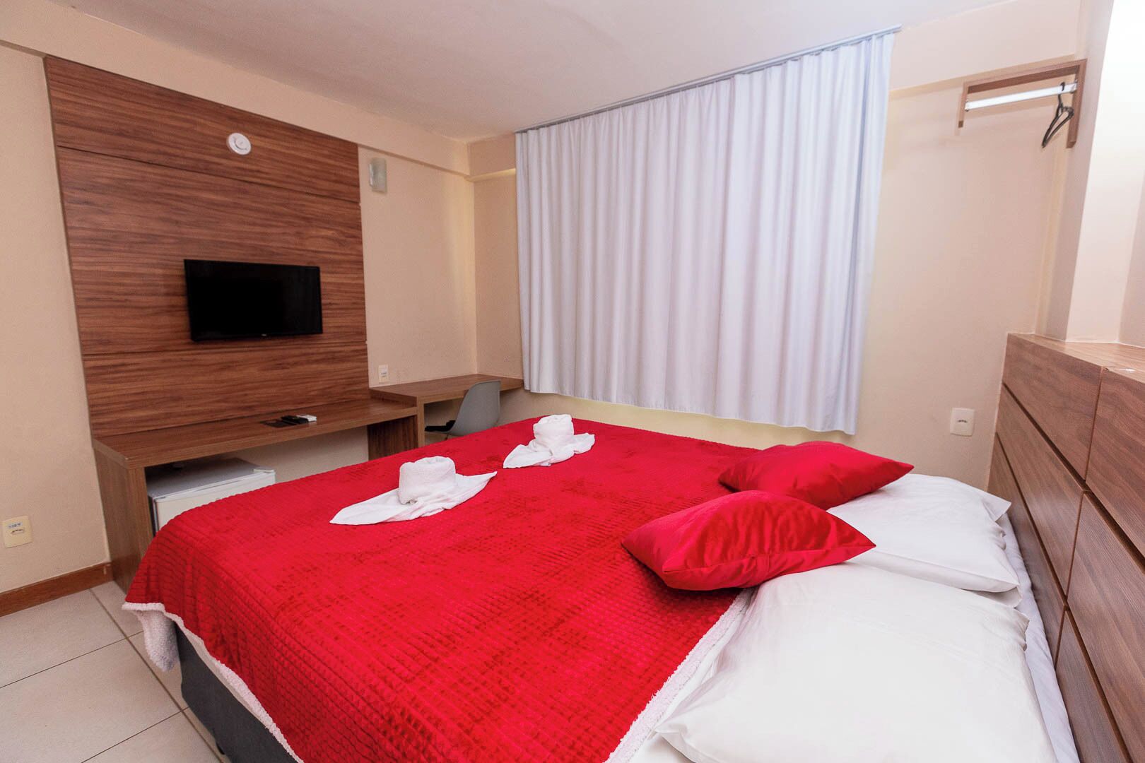 Hotelkamer met een groot bed, een aan de muur bevestigde televisie, een bureau en een raam met gordijnen.