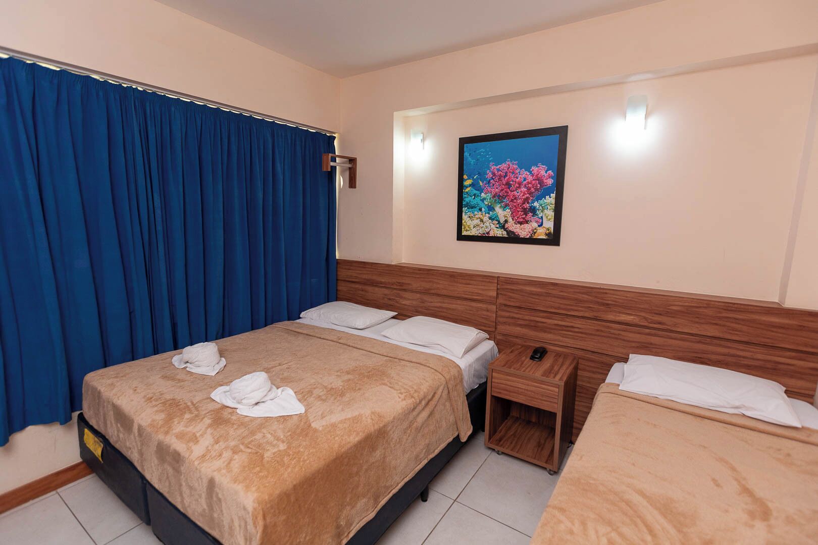 Une chambre d’hôtel avec un lit, une table de chevet, une tête de lit en bois, un rideau bleu et un tableau encadré au mur.
