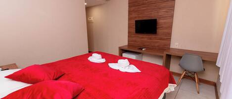 Una habitación de hotel con cama, escritorio, silla, televisor y aire acondicionado.
