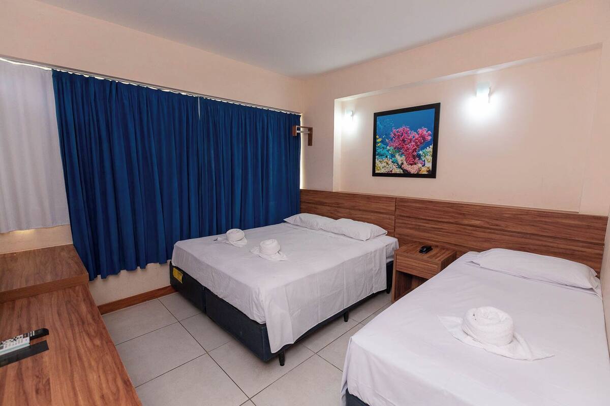 A hotel room with two beds, a wooden headboard, a desk, and a painting on the wall.