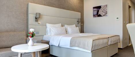 A modern hotel room with a large bed, a small round table, a sofa, and a painting on the wall.