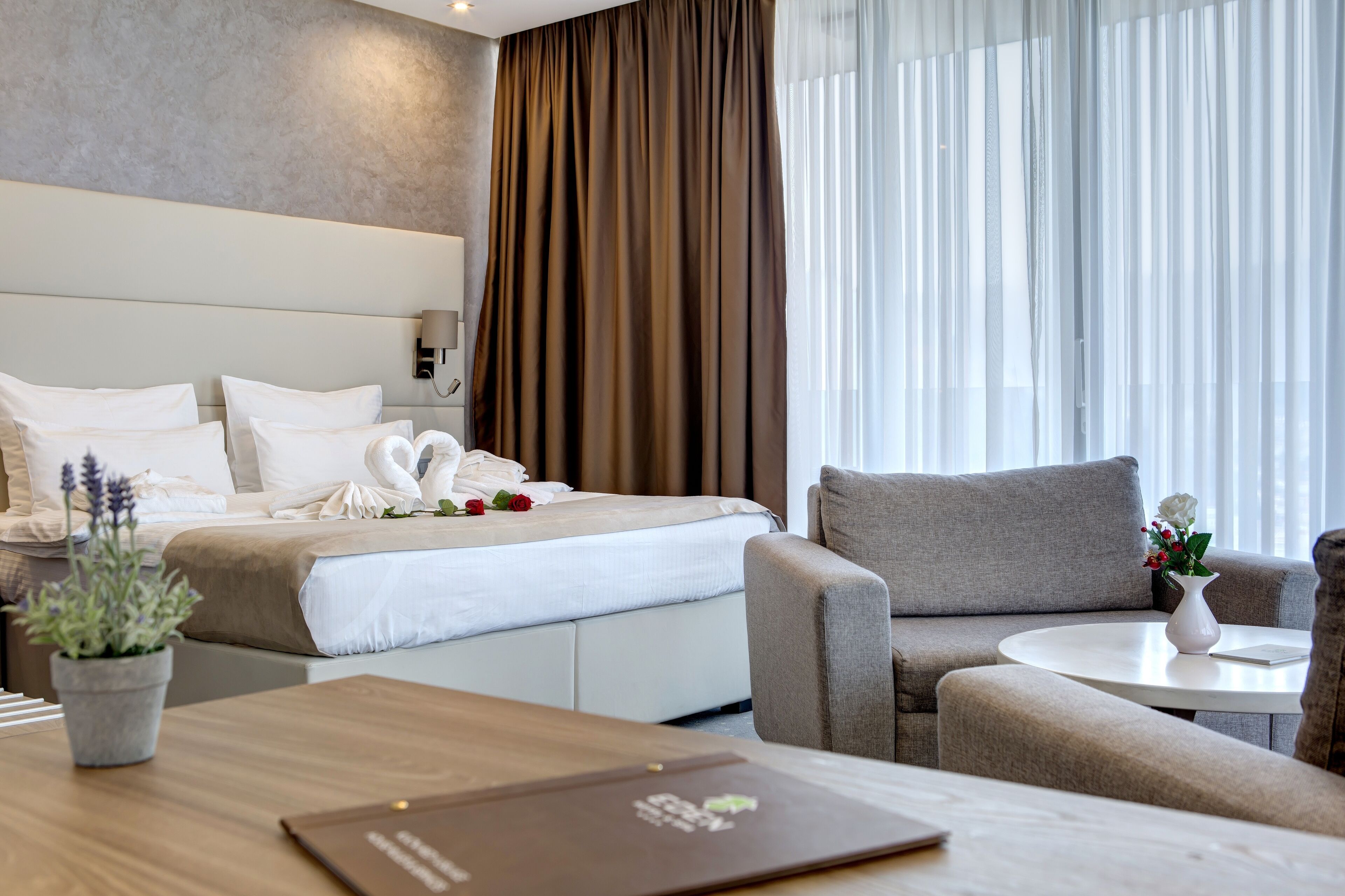 Quarto de hotel moderno com cama bem arrumada, sofá, mesa pequena e planta em vaso.