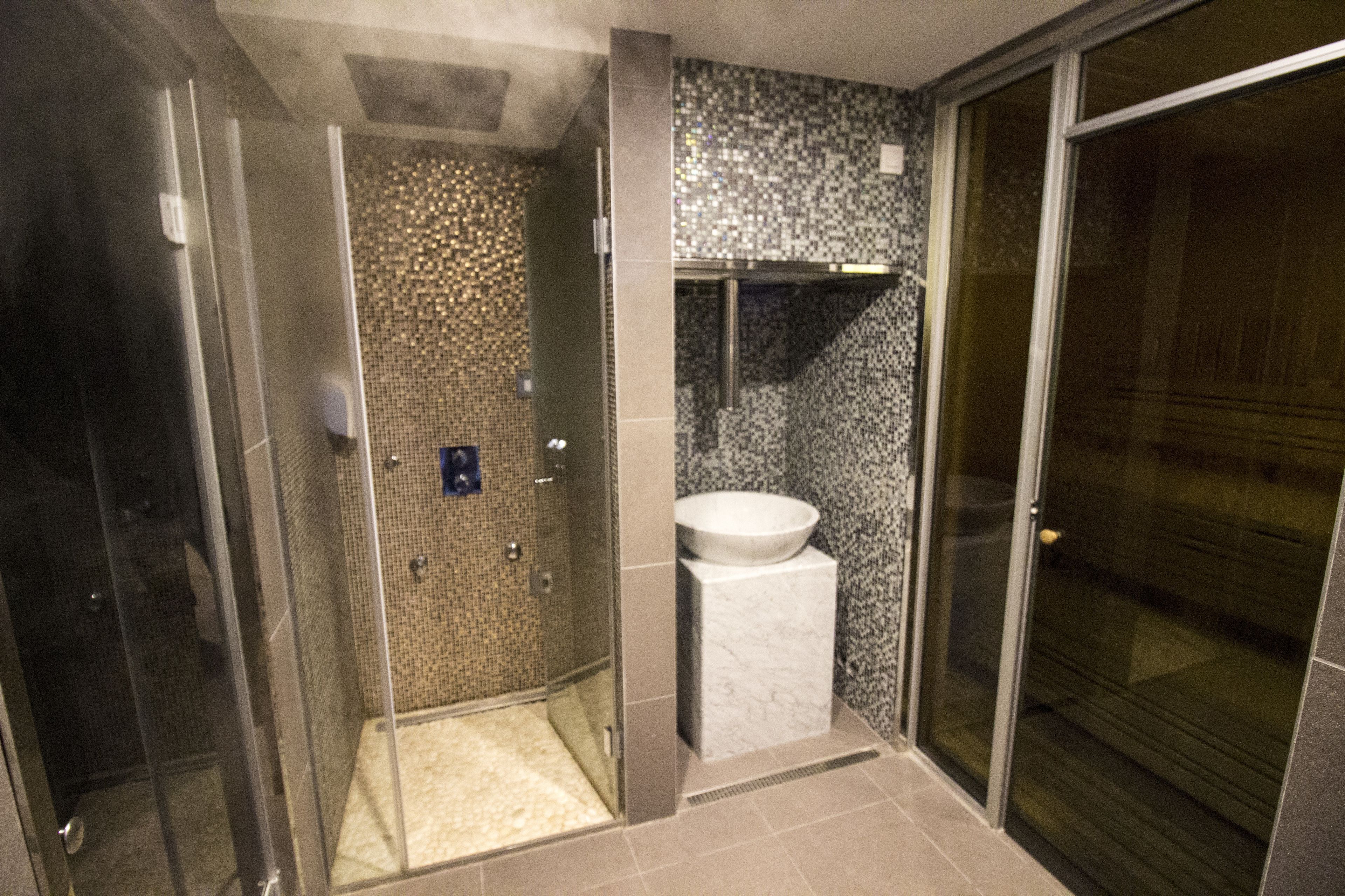 Een moderne badkamer met een douche met glazen wand, een marmeren wastafel en een betegelde douchewand.