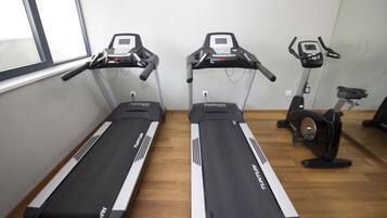 Two treadmills and an elliptical machine in a room with wooden flooring and a window.