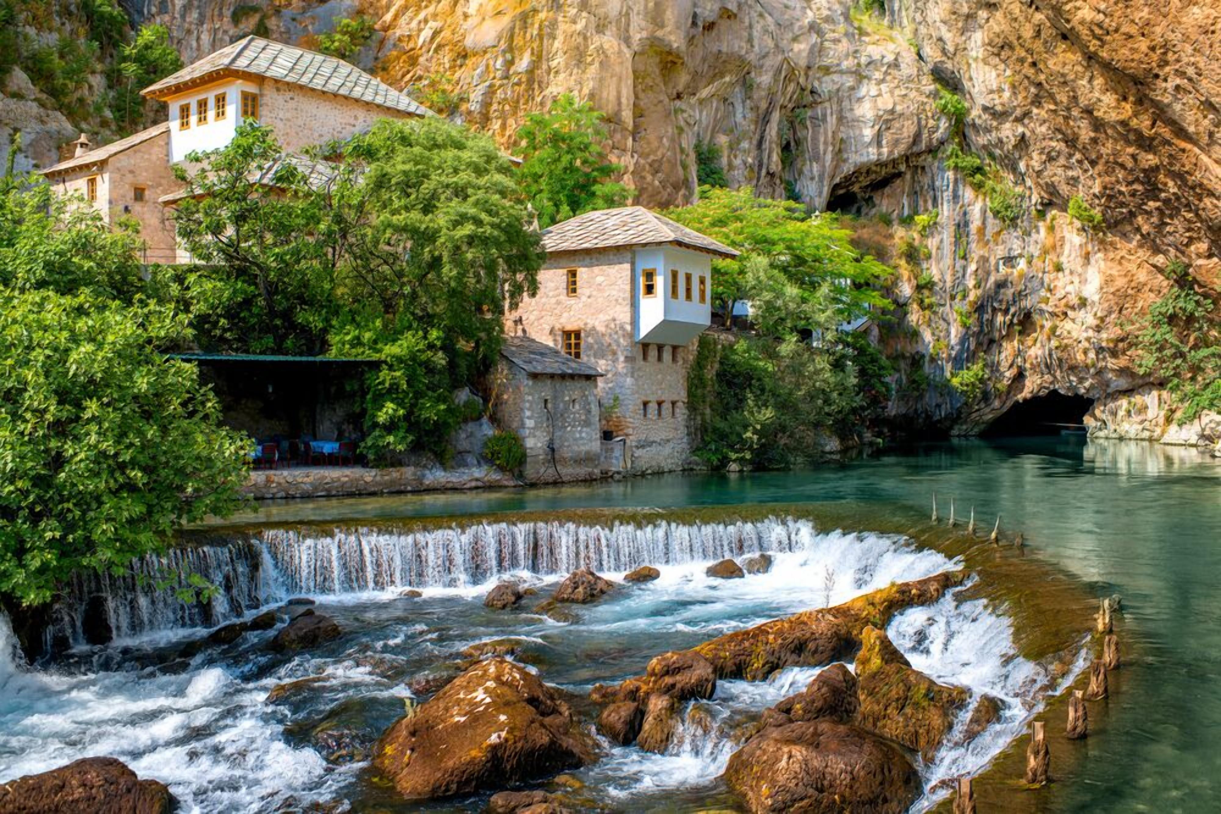A stone building with a small tower, a waterfall, and a river.