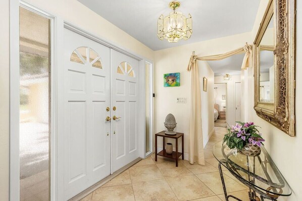A hallway with a white door, a glass table with flowers, and a chandelier. - Location, location, location! Without bridges and locks in the Gulf of Mexico! (Cape Coral)