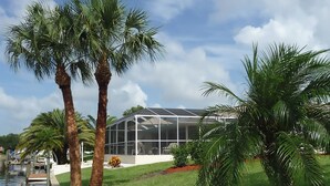 Una casa moderna con una serra in vetro, circondata da palme e una piscina.