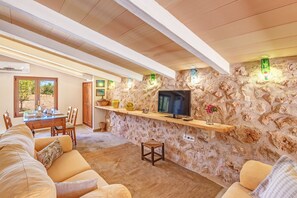 A cozy living area with a stone wall, a flat-screen TV, wooden furniture, and a dining table.