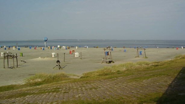A beach with a paved walkway leading to the water, several beach huts, and a lifeguard stand. - Vacation home in Dornumersiel 80-142b - 800-142b (Dornum)