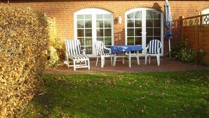 A patio with a brick wall, two windows, and a table with chairs. - Vacation home in Dornumersiel 80-142b - 800-142b (Dornum)