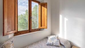 A room with a window, a bed with patterned bedding, and a view of trees outside.