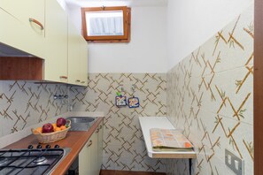 A kitchen with a gas stove, a sink, a window, and patterned tiles.