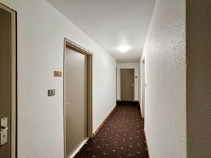 A narrow hallway with carpeted flooring, white walls, and doors leading to rooms.